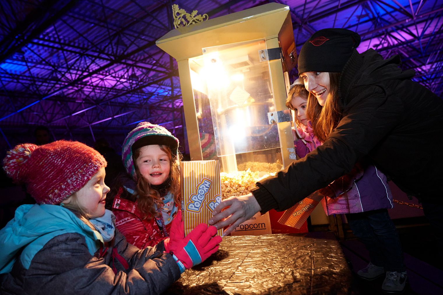 Mehrere Kinder in dicken Wintersachen nehmen eine Popcorntüte entgegen.