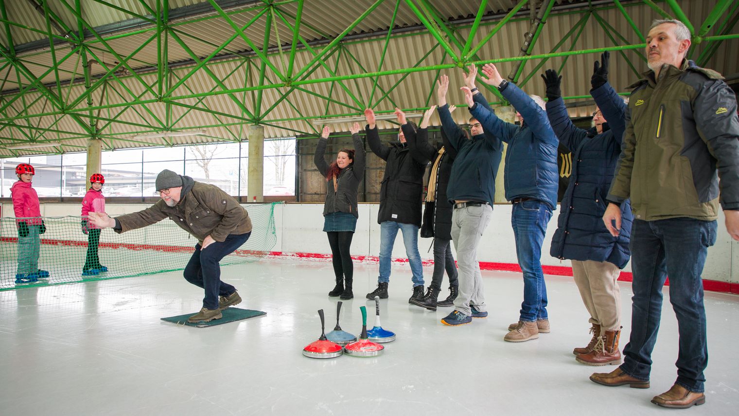 Eine Gruppe beim Eisstockschießen, einer wirft den Eisstock und die anderen jubeln.