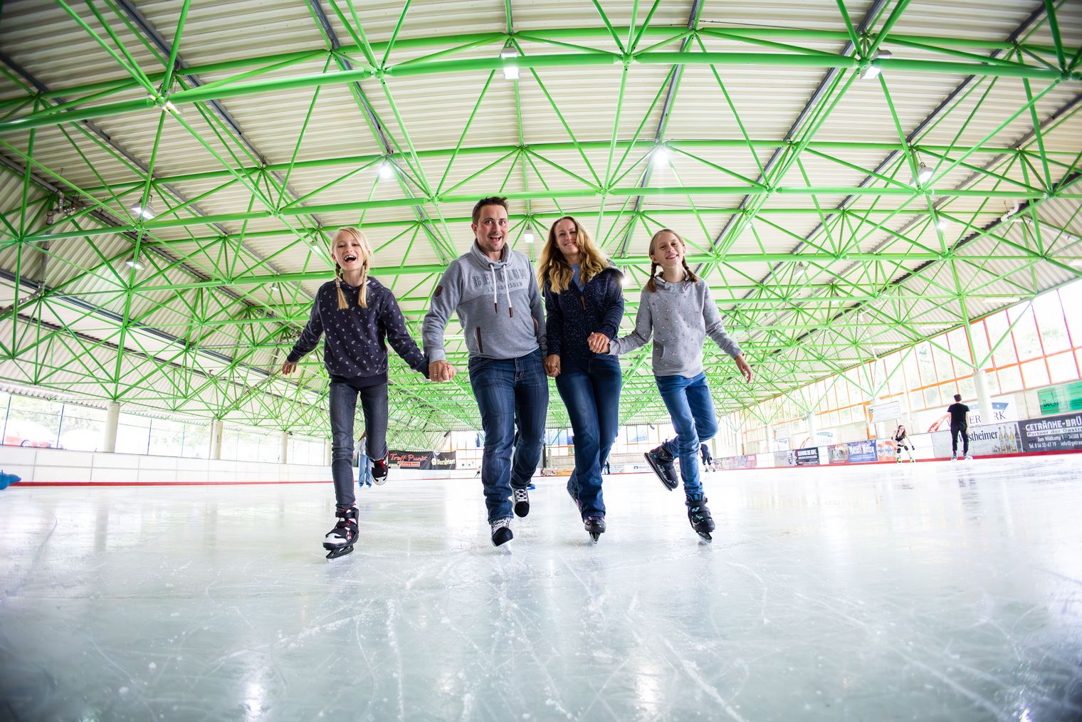 Familie läuft gemeinsam Schlittschuh auf der Eisfläche.
