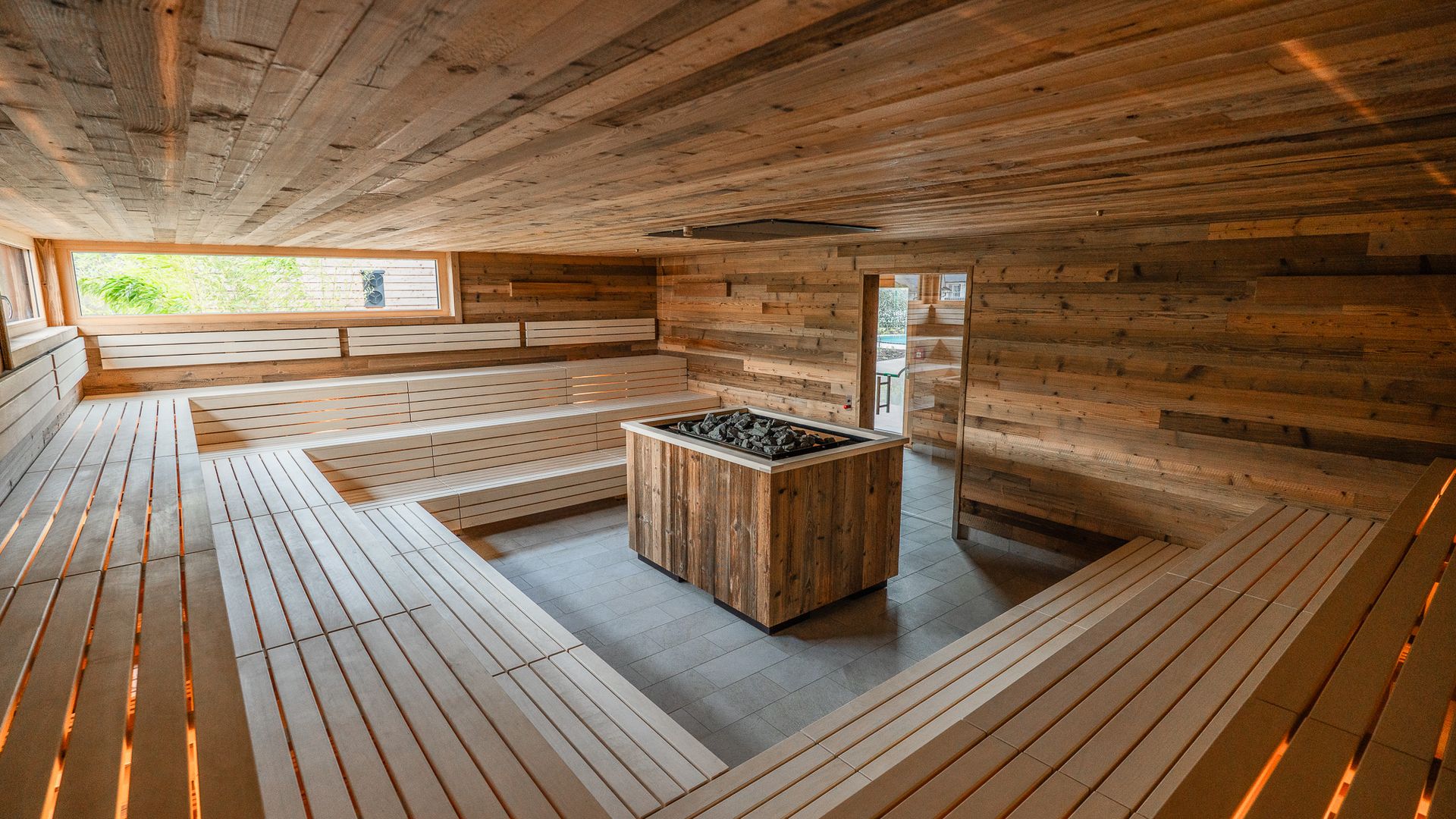 Orenbergsauna mit beleuchteten Saunabänken und großem Saunaoffen in der Mitte.