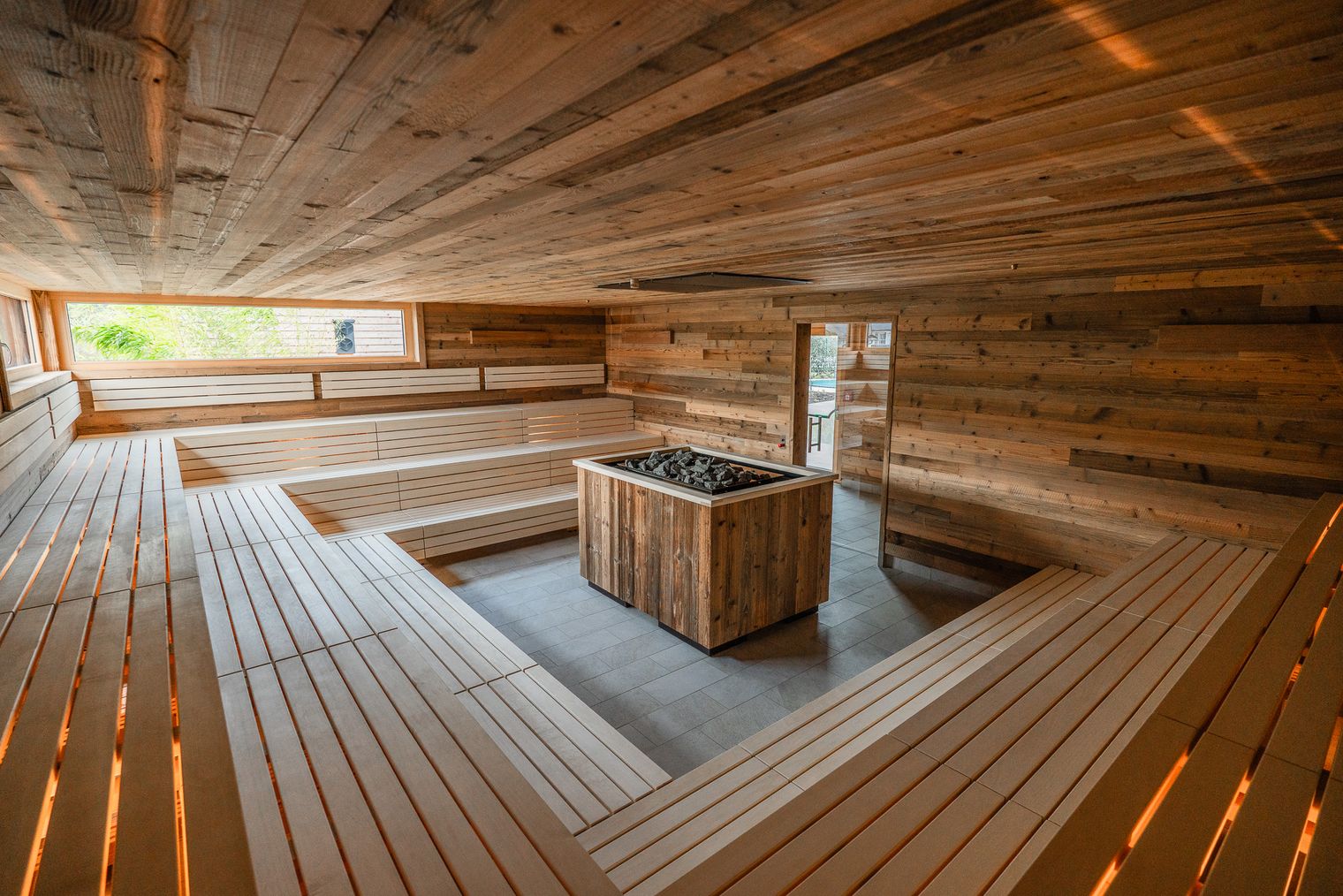 Orenbergsauna mit beleuchteten Saunabänken und großem Saunaoffen in der Mitte.